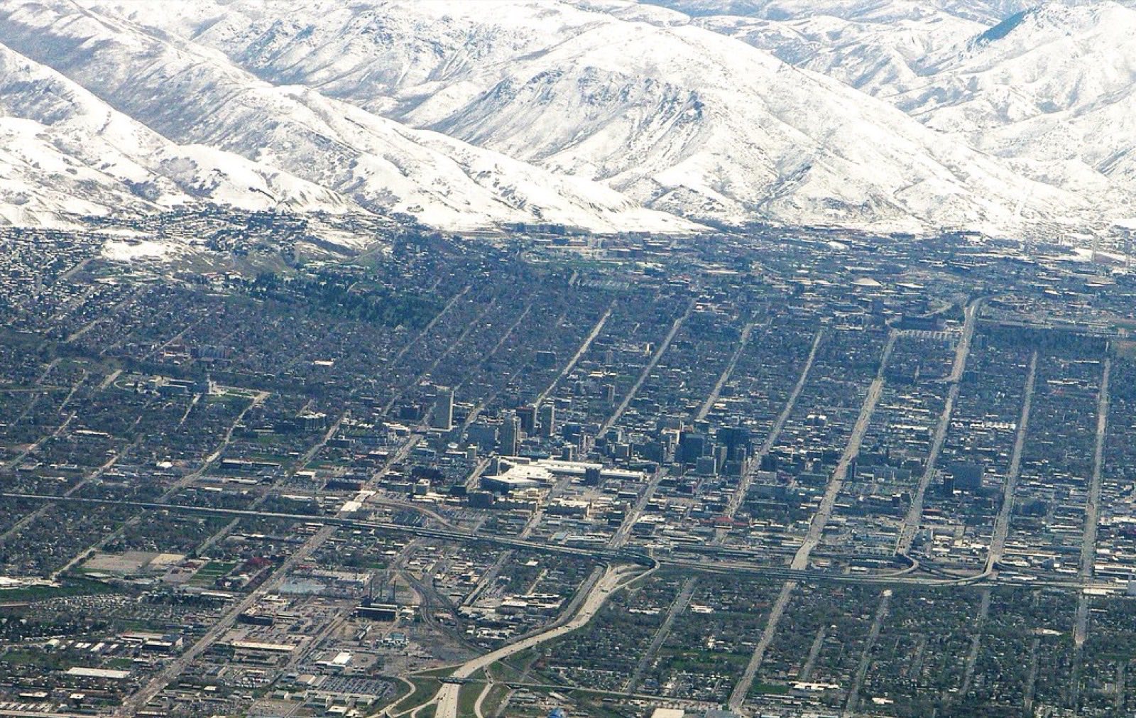 Salt Lake City laid out on its grid at the foot of the snow-covered Wasatch Range, seen from the air in early spring.